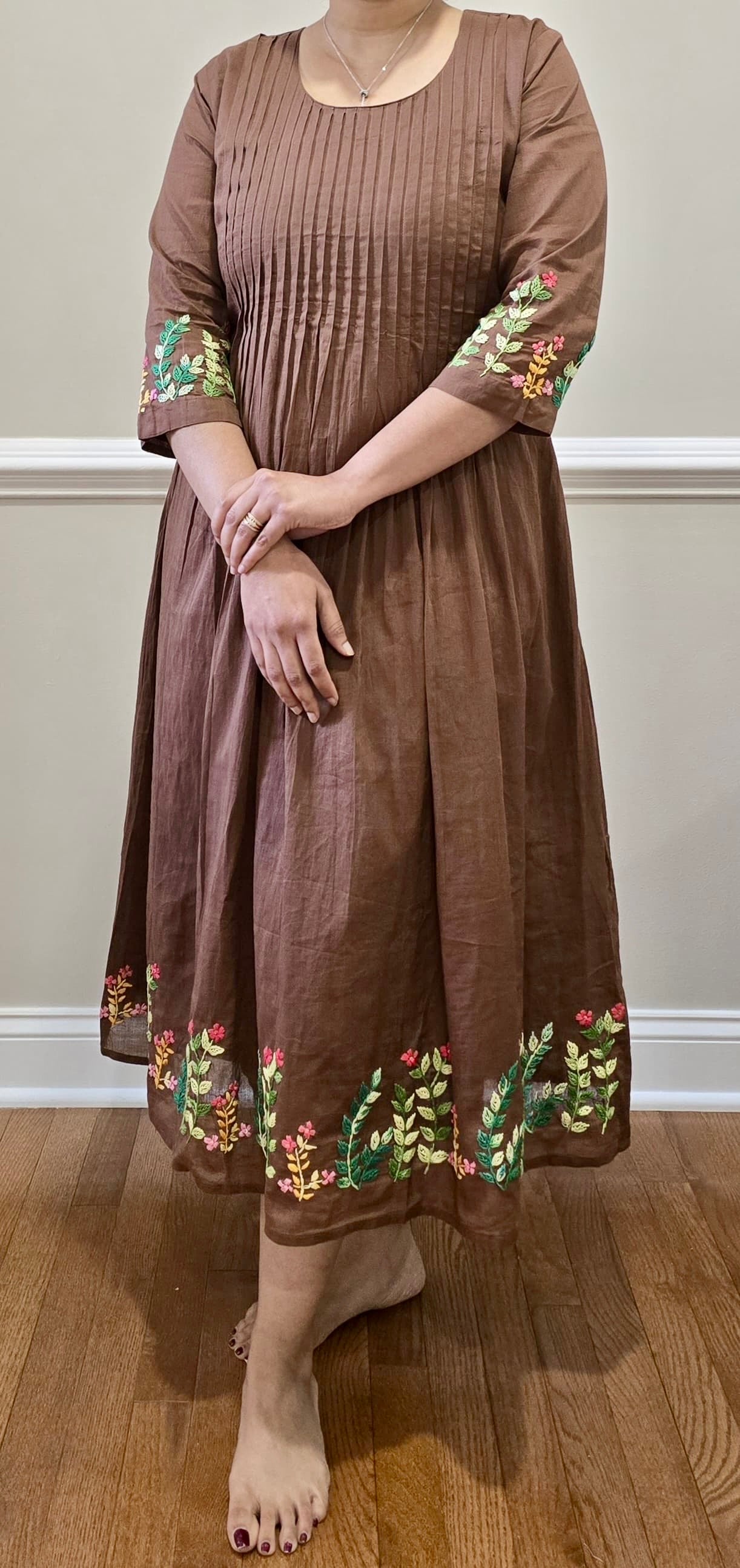 Brown dress with floral embroidery on sleeves and hem against a neutral background